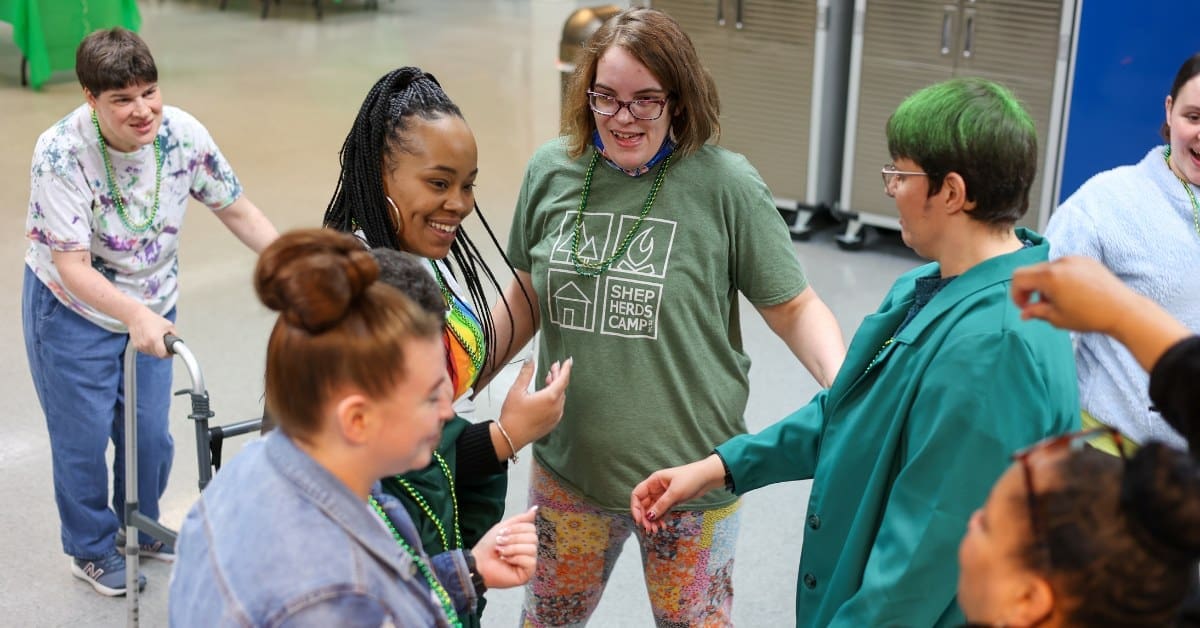 A group of individuals celebrates together in a circle, sharing a joyful moment at the TLC Day Program.