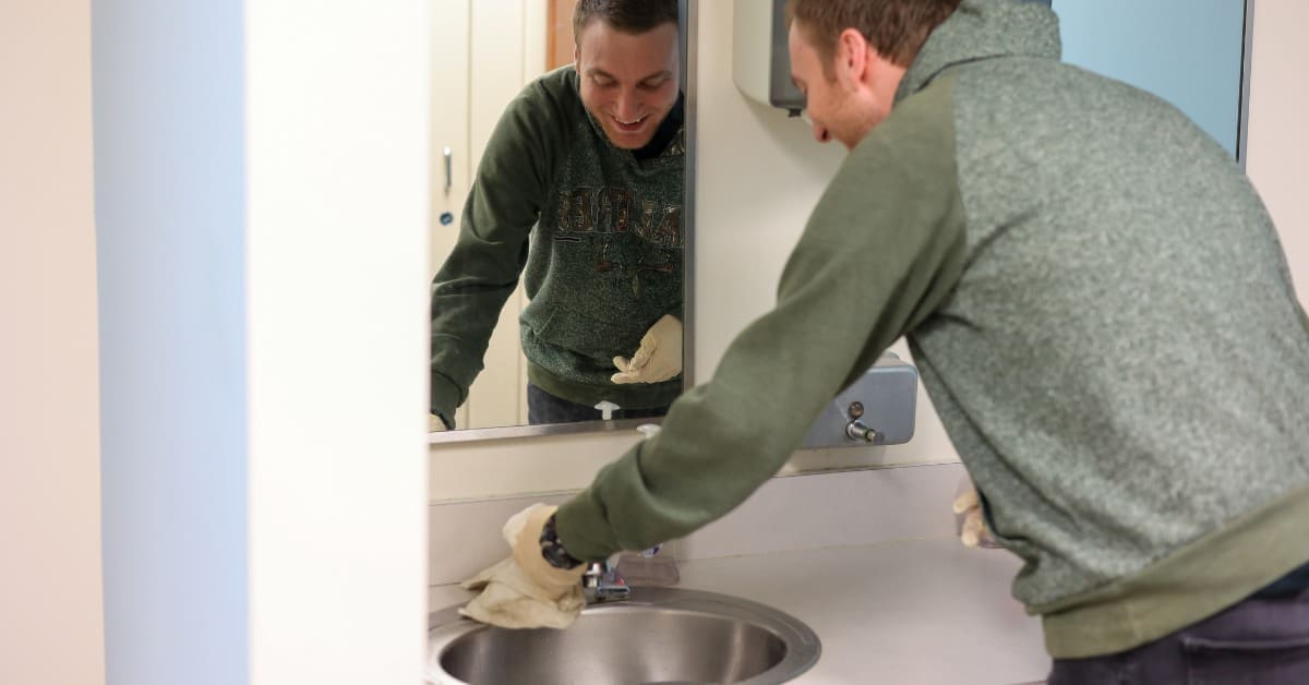 A TLC individual cleans a sink with a rag.