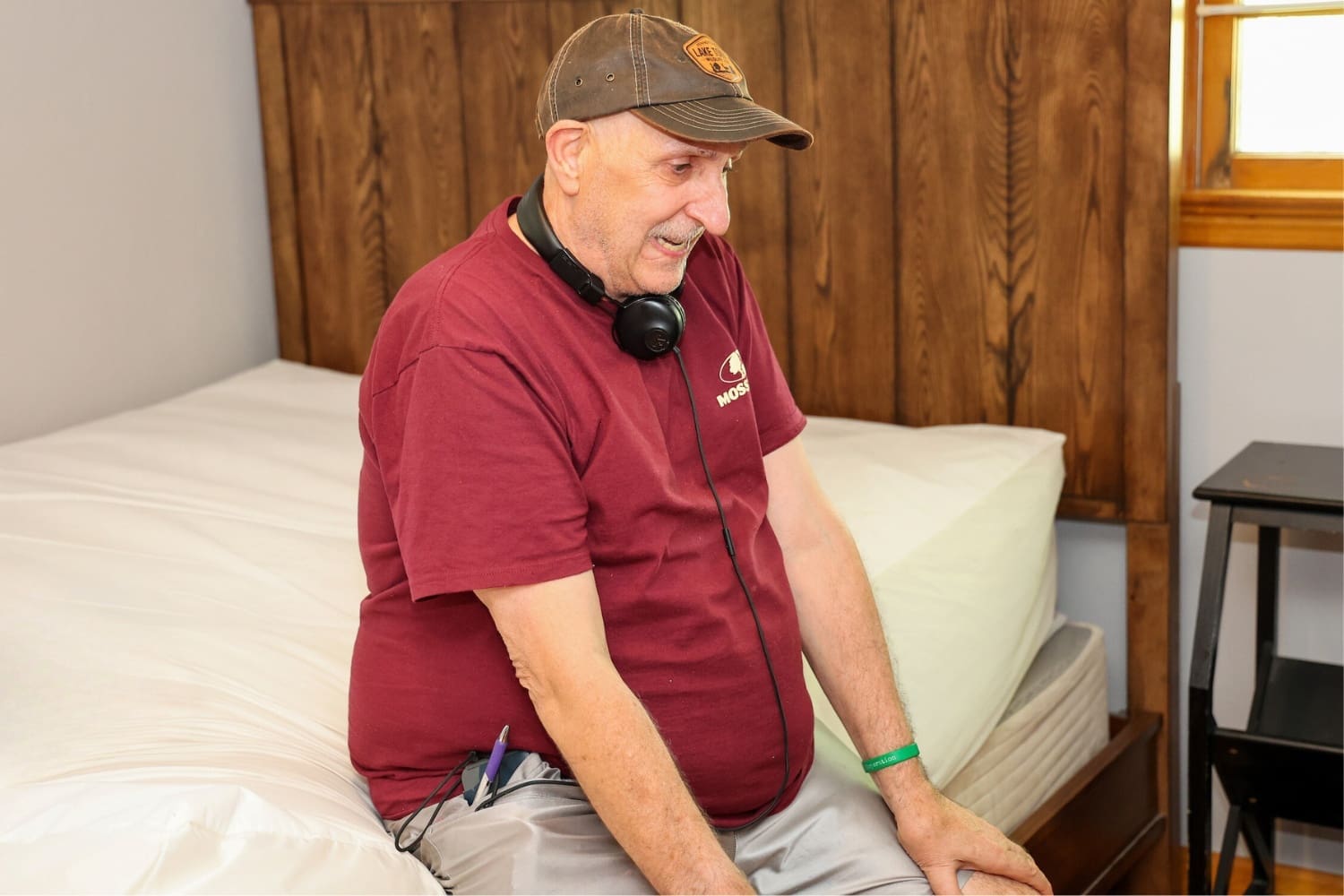 A TLC individual sits on a bed in his residence.