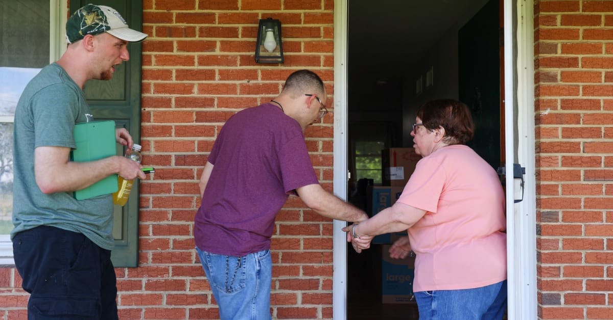 A TLC Direct Support Professional guides two individuals through the door of their residence.