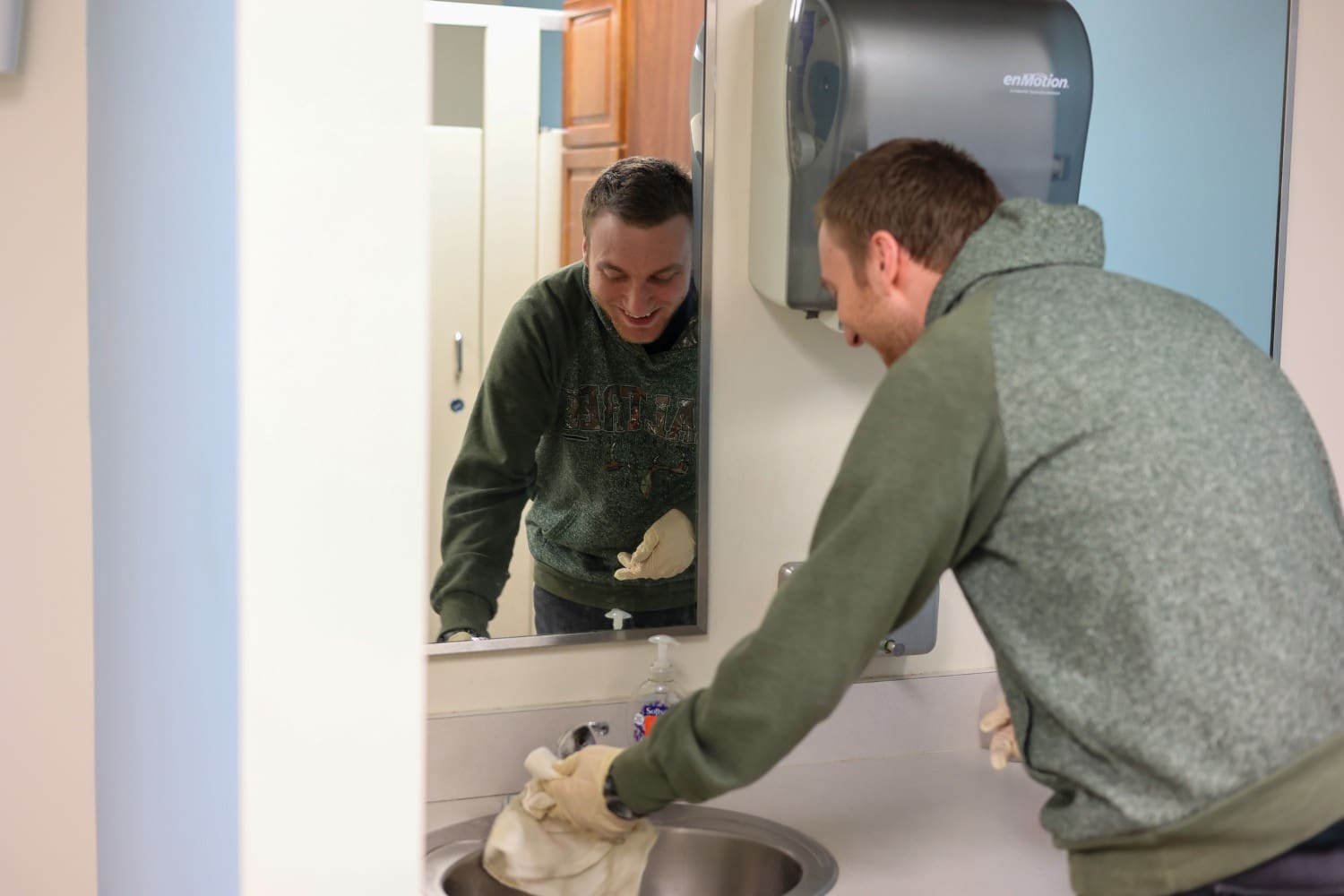 A TLC individual cleans a sink with a rag.