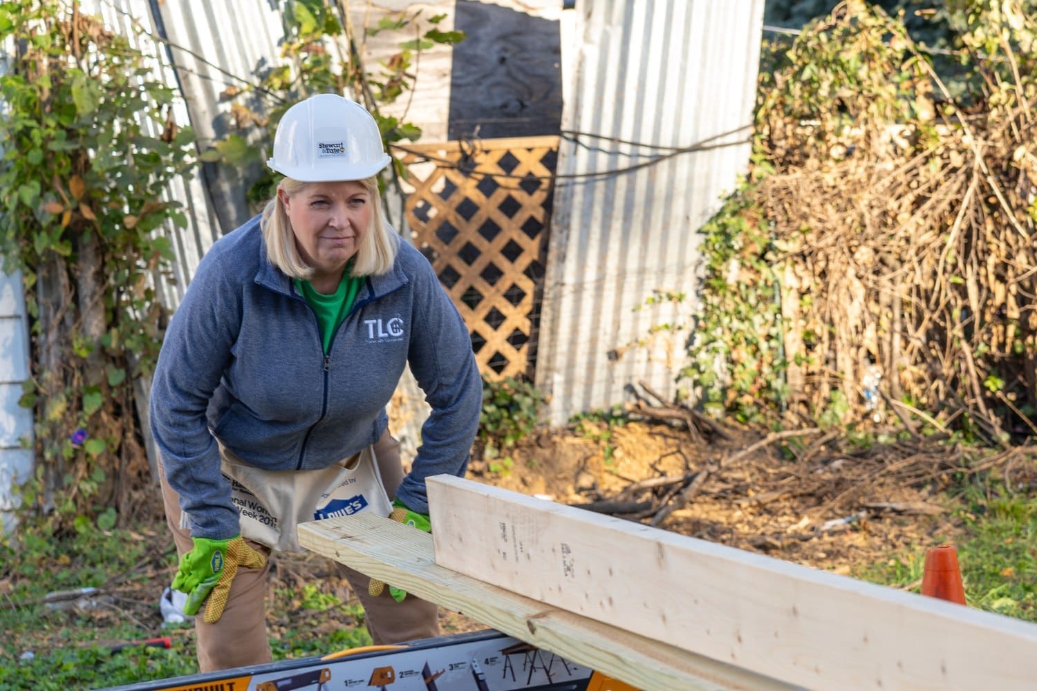 A TLC volunteer in a hard hat and gloves works on a construction project, positioning a wooden beam at a Habitat for Humanity site.