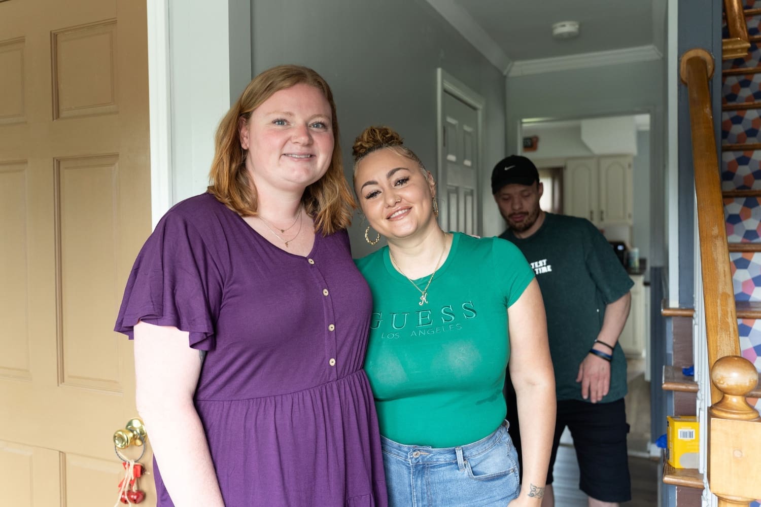 TLC Residential Manager Danielle “Dani” Ford (left) and Direct Support Professional Kayla Powell (right) stand together in the doorway of a TLC home while Ryan smiles in the background.