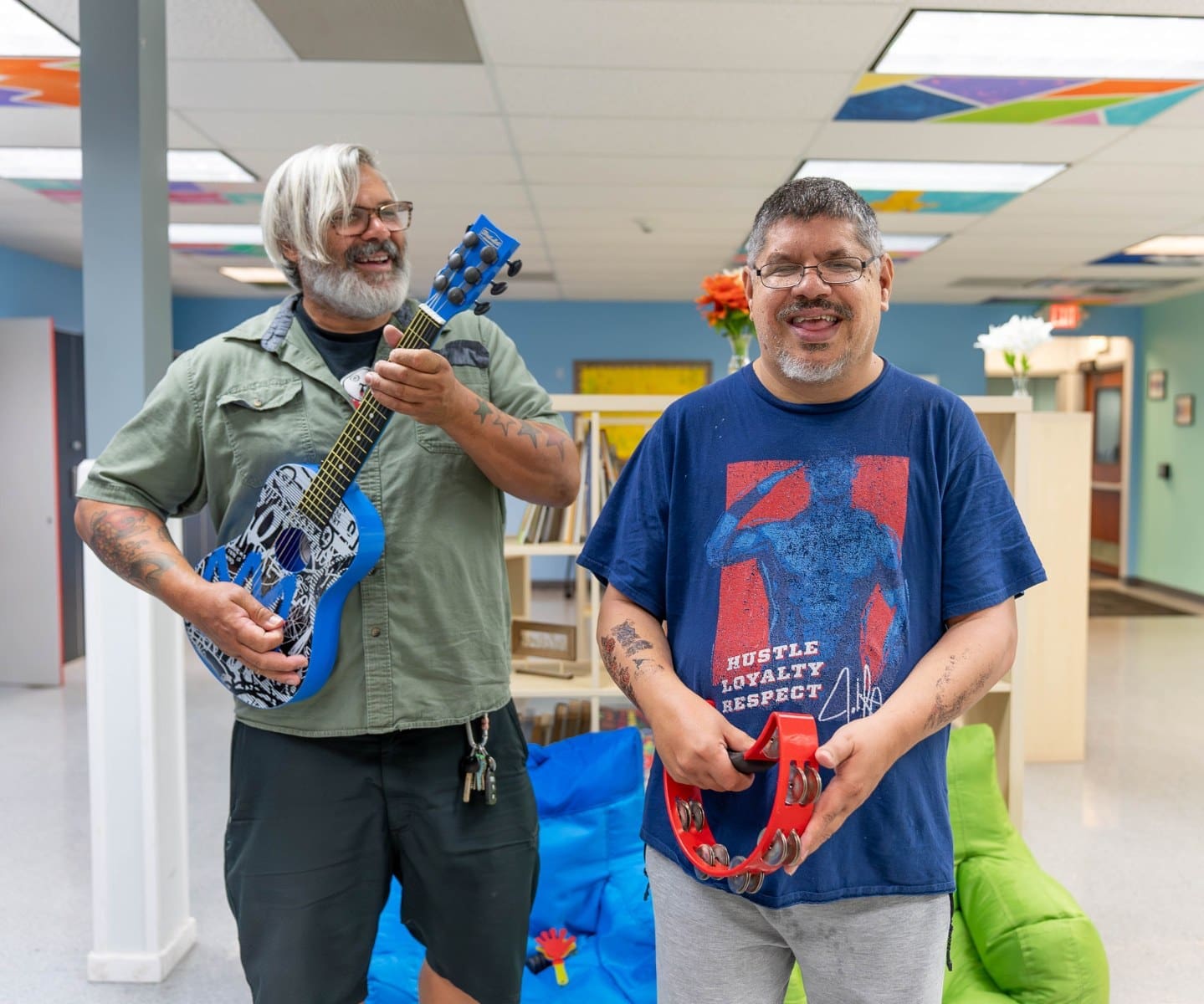 A TLC employee plays a guitar next to a TLC individual playing a tambourine during an indoor music party.